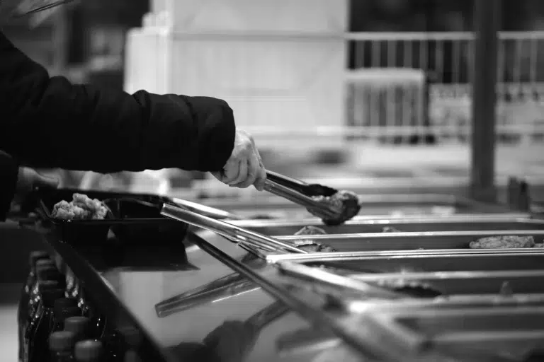 Personne se servant de la nourriture chaude à l’aide d’une pince dans un buffet en libre-service