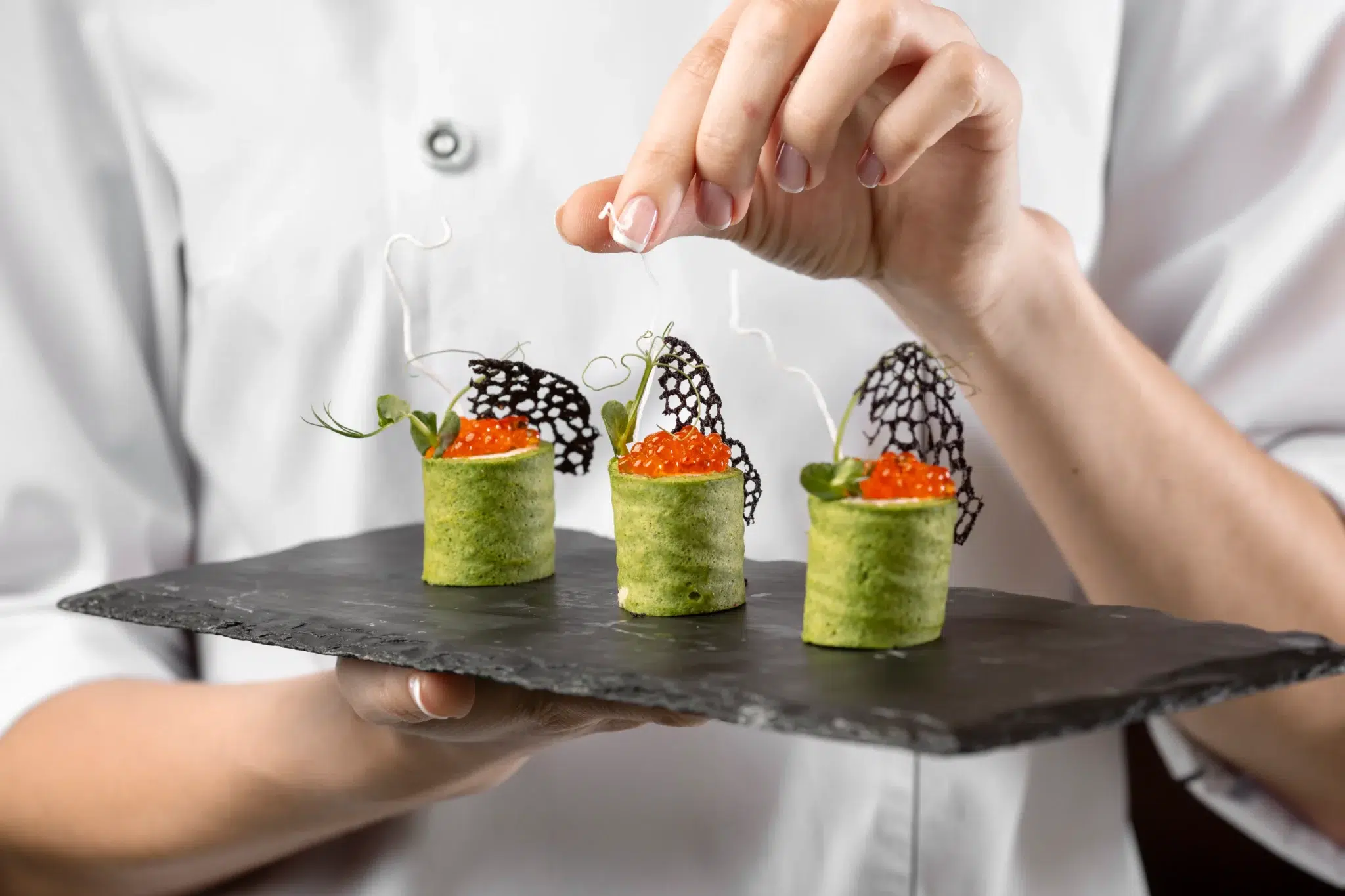 Un chef en tenue blanche dresse avec précision des bouchées raffinées sur une ardoise noire, illustrant le savoir-faire d’un traiteur sur mesure